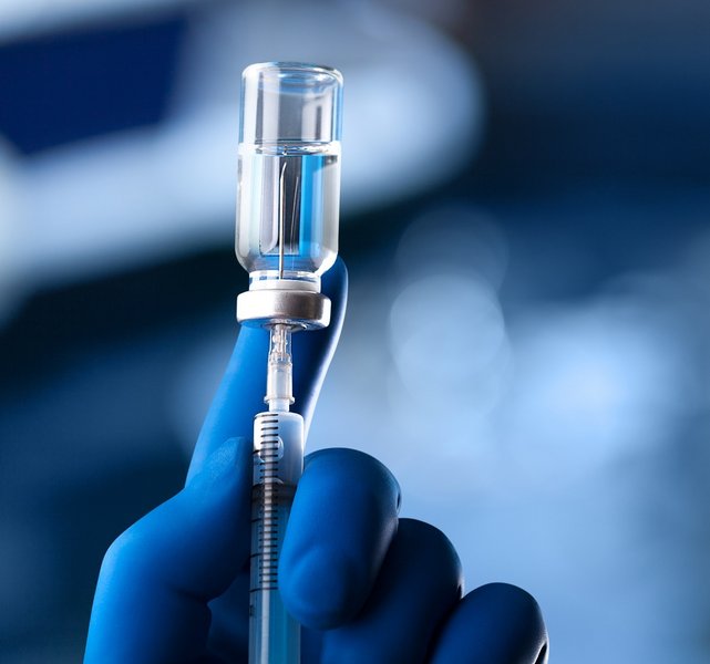 A medical hand in a glove holds an ampoule with a vaccine and a syringe with illustration A medical hand in a glove holds an ampoule with a vaccine and a syringe with illustration