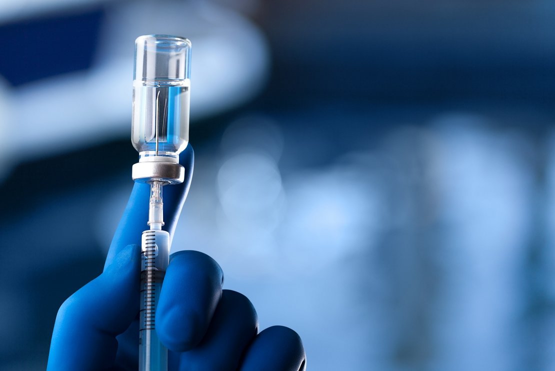 A medical hand in a glove holds an ampoule with a vaccine and a syringe with illustration A medical hand in a glove holds an ampoule with a vaccine and a syringe with illustration